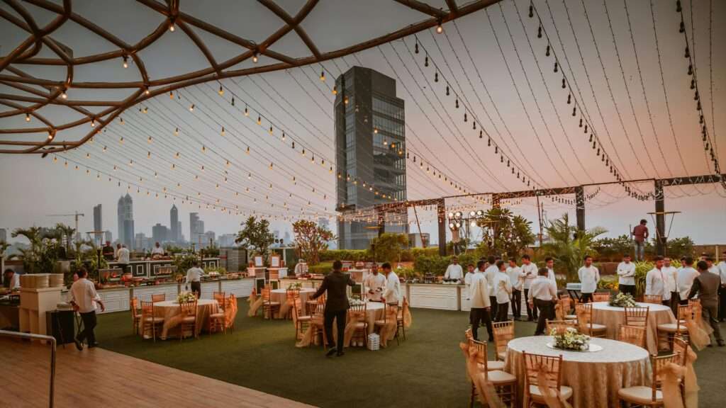 Rooftop event venue with elegant decor, string lights, and a city skyline view at sunset